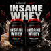 Two containers of Insane Labz Insane Whey protein powder with birthday cake and cookies & cream flavors on a dark background.